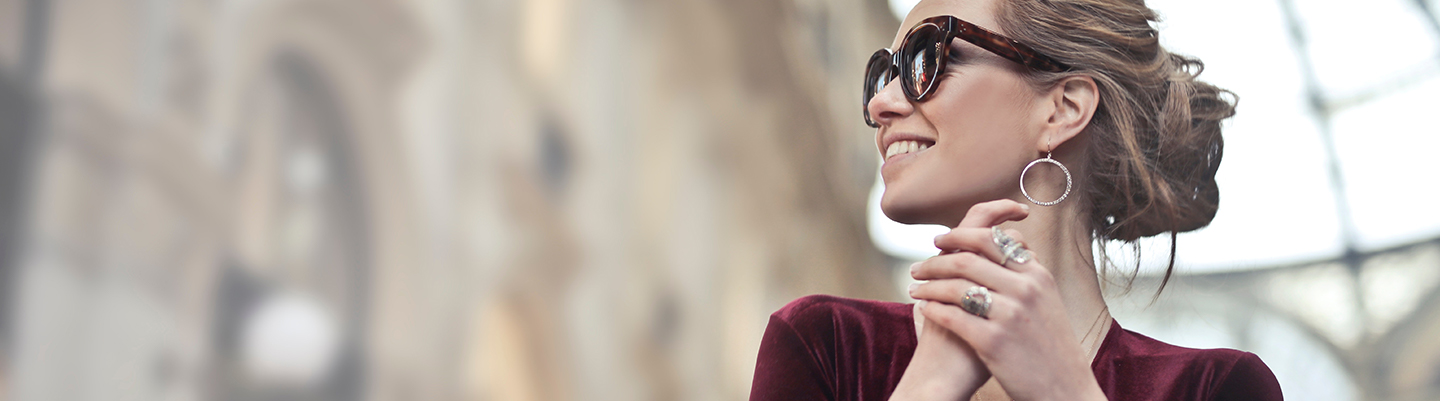 Foto einer eleganten Frau mit Sonnenbrille, Ohrringen und Schmuck, die erfreut lächelt